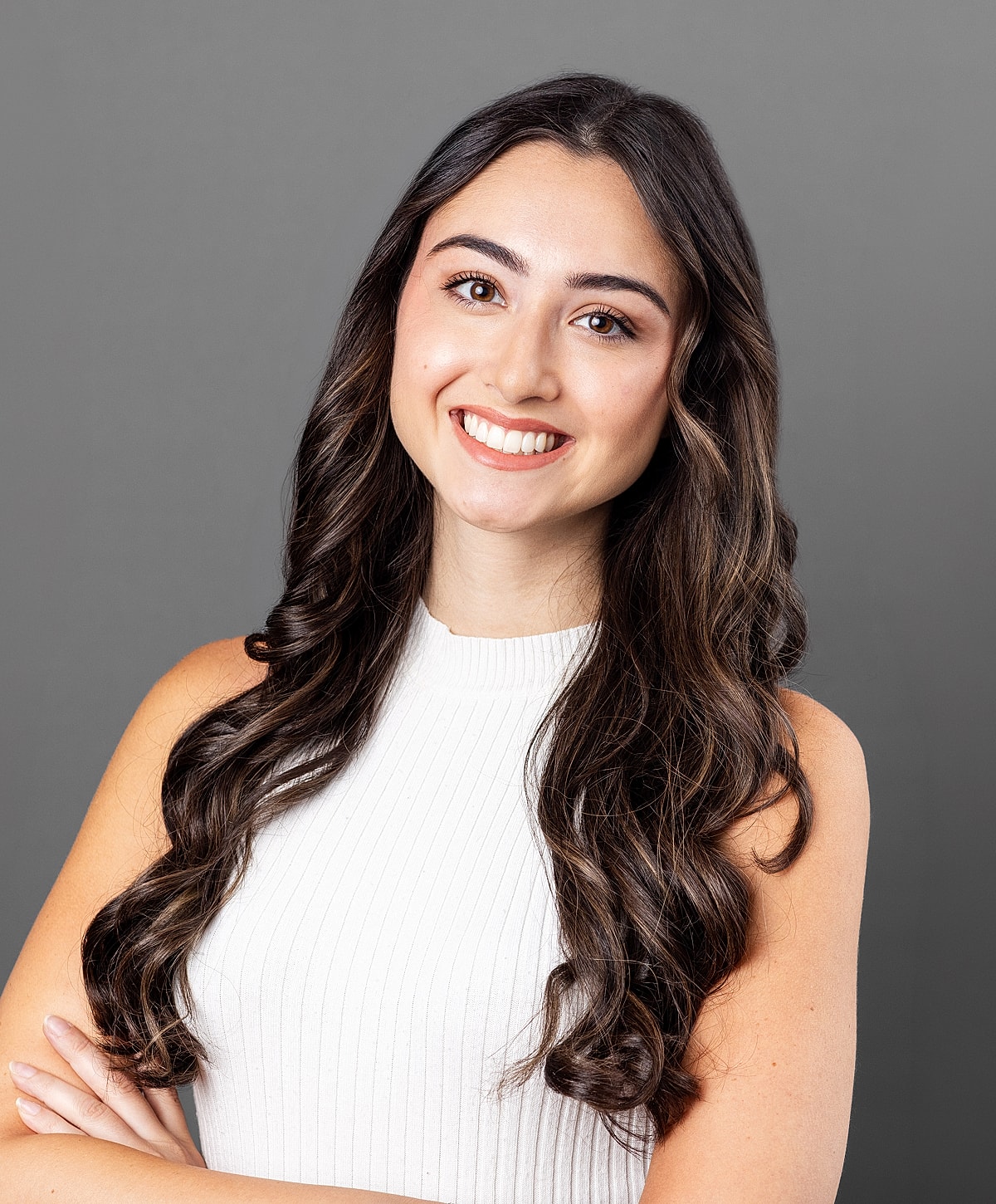 Smiling woman with long, wavy hair, gray background.