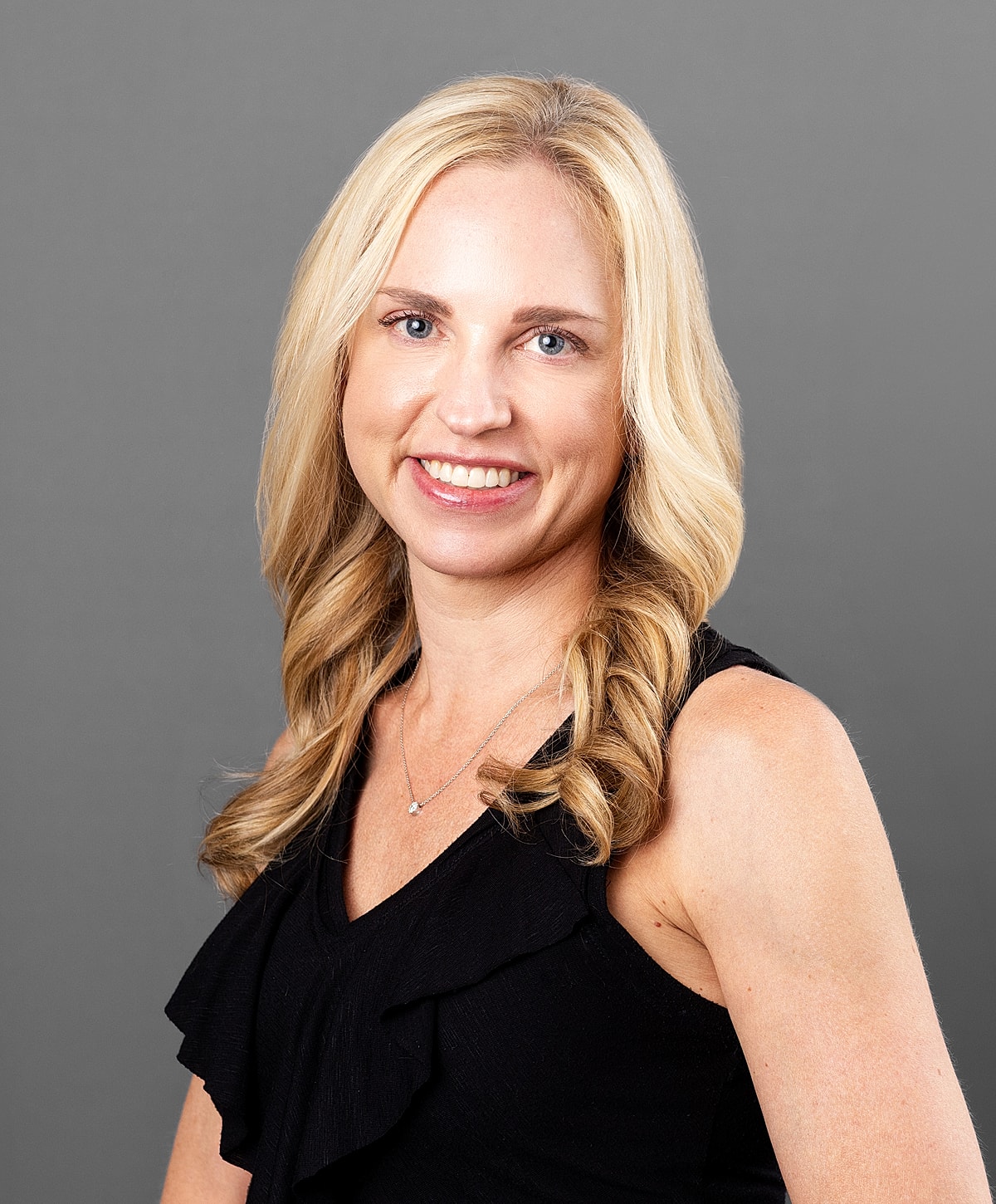 Smiling woman with blonde hair against gray background.