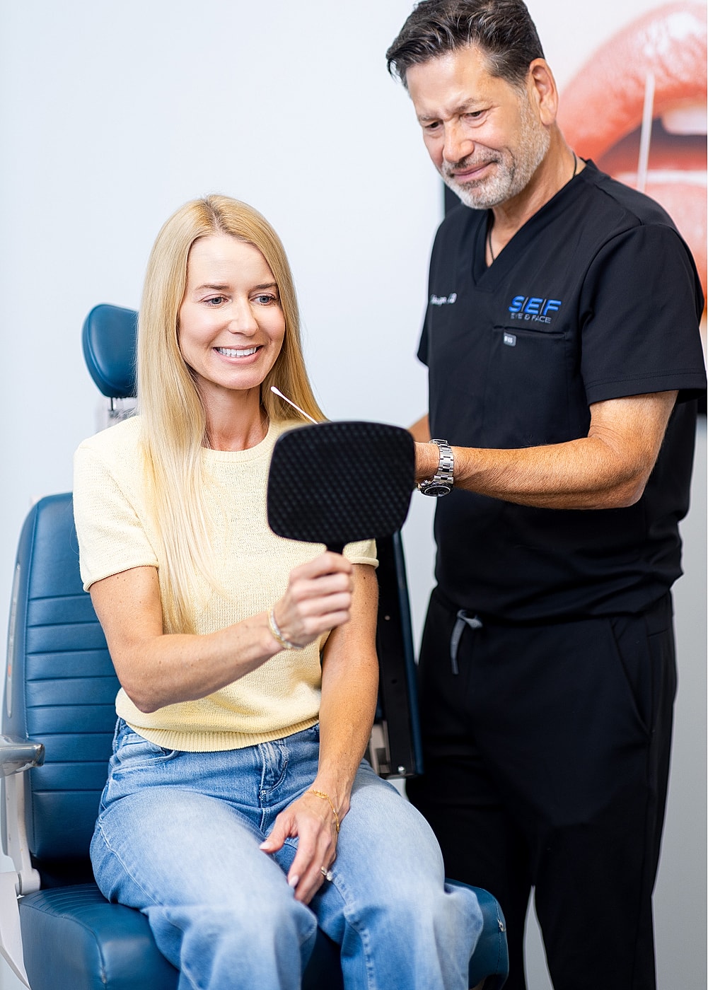 Patient smiling while looking in mirror with doctor.