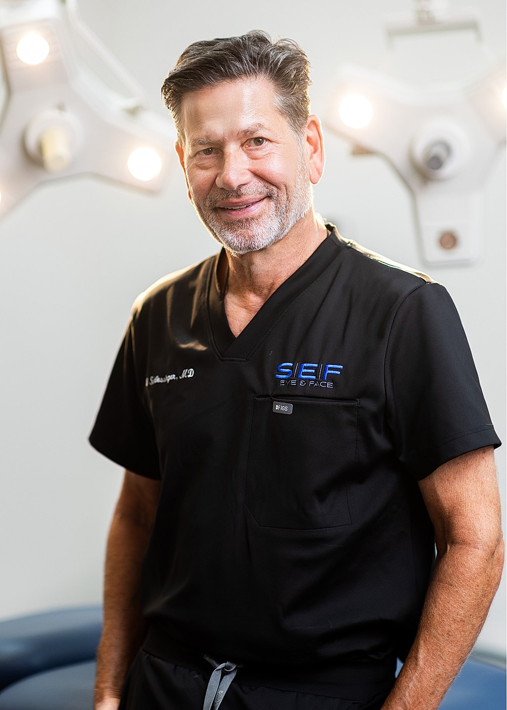 Male doctor in surgical scrubs, smiling confidently.