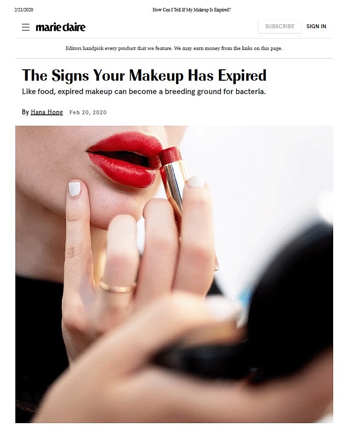 Applying red lipstick while looking in a mirror.
